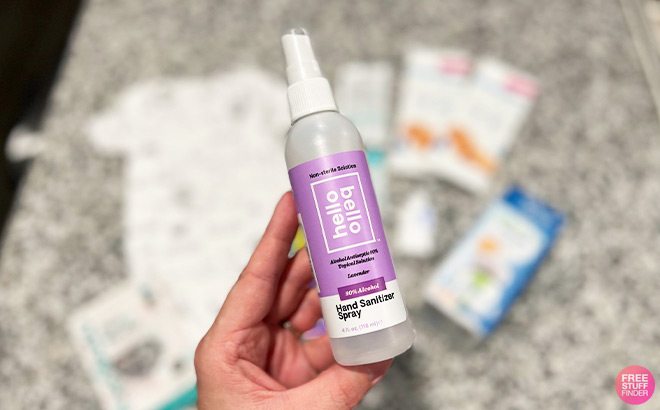 Hand Holding a Hello Bello Hand Sanitizer Spray in Front of a Table Top Hand Holding a Hello Bello Hand Sanitizer Spray in Front of a Table Top
