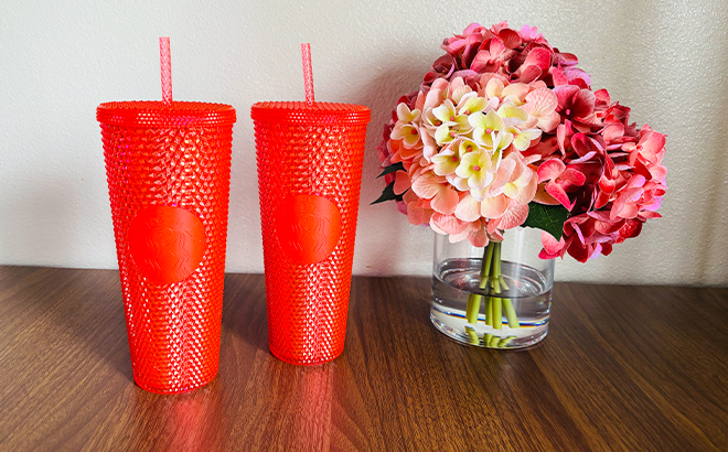 Two Red Starbucks Tumblers Next To a Vase with Flowers Two Red Starbucks Tumblers Next To a Vase with Flowers